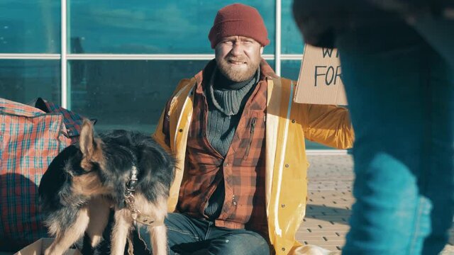 A homeless man with a dog is asking for a job in the street