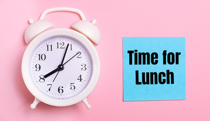 On a light pink background, a white alarm clock and a blue sheet of paper with the text TIME FOR LUNCH
