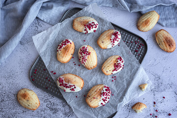 homemade cookies: madeleine cookies with raspberry slices in a white chocolate glaze on a gray background