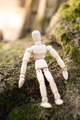 Small wooden mannequin doll siting on a tree with the moss in the forest