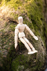 Small wooden mannequin doll siting on a tree with the moss in the forest