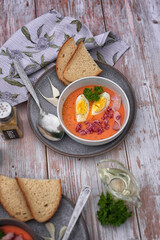Cold tomato soup or gazpacho. Cold Spanish salmorejo soup made of tomatoes, bread, garlic and olive oil. Serving in a gray ceramic dish on a light wooden background. Summer cold vegan food/
