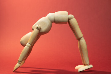 Wooden mannequin  staying in Standing Forward Bend Pose, Intense Stretch Pose, doing yoga Asana - Uttanasana, picture on red background


