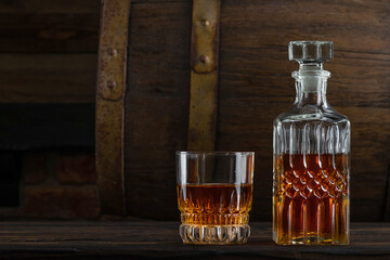 Glass decanter with whiskey, brandy on a vintage background of a rustic oaken barrel. Alcoholic beverage. Still life in the old style