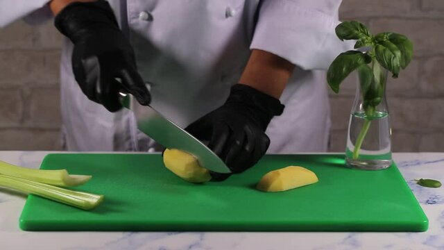 A chef woman cuts potato with knife into slices.