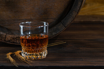 Glass decanter with whiskey, brandy on a vintage background of a rustic oaken barrel. Alcoholic...