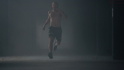 Active sportsman doing physical exercises. Male jogger running in dark corridor