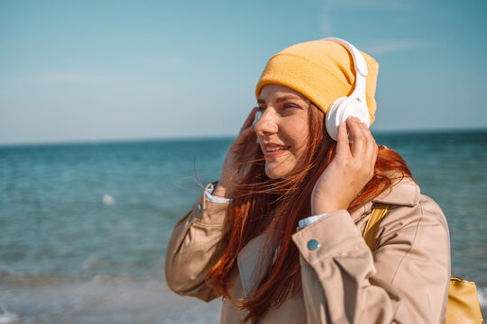 Beautiful joyful smiling young woman meditating listening to smartphone music phone app with white bluetooth headphones on beach