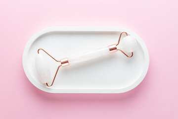 Pink Guasha massage tool on white concrete tray on pink background. Rose quartz jade roller. Skin care at home, anti-aging and lifting therapy. Top view. Copy space.