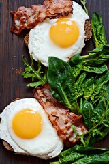 Breakfast fried eggs with bacon, fresh spinach, arugula on wooden board. 
