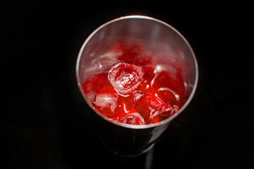 Red cold syrup with ice in a tool for mixing and making alcoholic cocktails shaker on a black background, close-up
