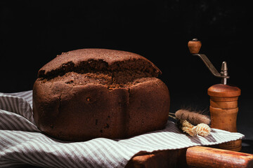 Freshly baked brown rye bread on wooden cutting board on black background