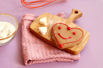 Heart shaped gingerbread on a cutting board, kitchen napkin, sugar cubes, flour in a cup, pastel background