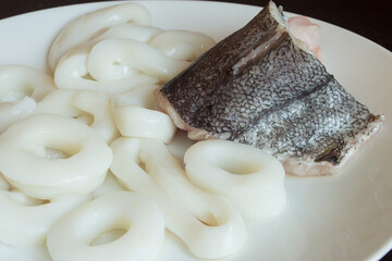 A piece of fresh hake with squid on the background on a white plate. Healthy cooking and fish.