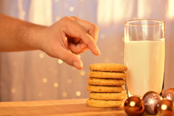 Mano masculina con leche con galletas, luces y esferas navideñas