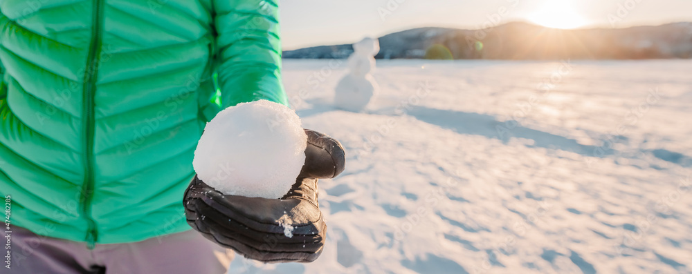 Poster Winter snowball fight concept outdoors. Girl holding snowball on snowy day with snowman in background on frozen lake at beautiful winter sunset living active lifestyle. Panoramic banner