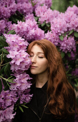 a red-haired girl of European appearance with freckles stands near the gray. bouquets of beautiful lilacs behind a girl. spring flowers. International Women's Day