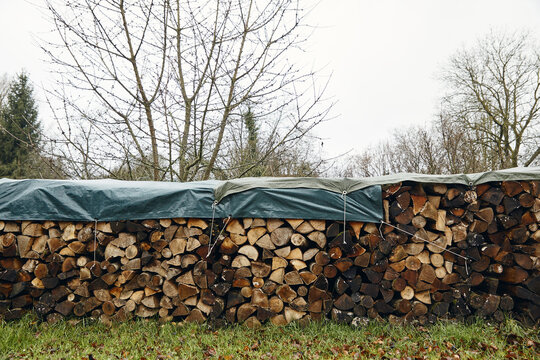 fagots de bûches de bois protégés par une bâche en plastique dans un jardin en hiver  