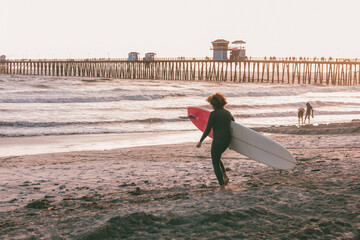 Woman carrying surfboard at sunset by pier