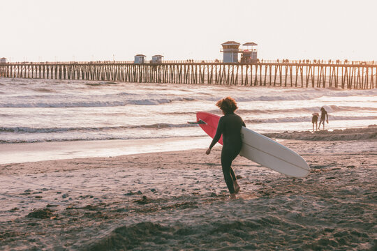 Woman carrying surfboard at sunset by pier