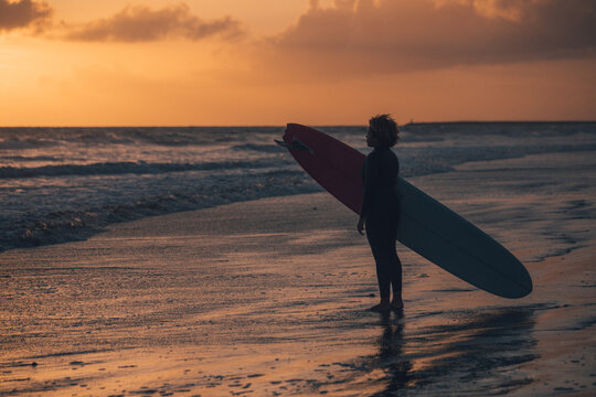 Woman carrying surfboard at sunset by pier