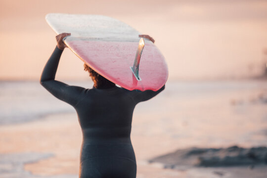 Woman carrying surfboard at sunset by pier