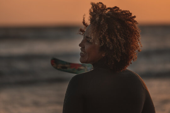 Woman carrying surfboard at sunset by pier