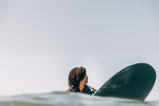 Black Woman sitting on her surfboard in the water