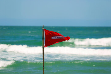 Red flag lifeguard danger warning sign on the beach. No swimming it's forbidden symbol, dangerous...