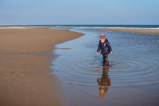 Small child makes ripples in water at beach on sunny winter day