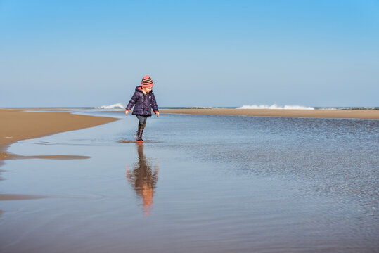 Small child walks in water at beach on sunny day in winter