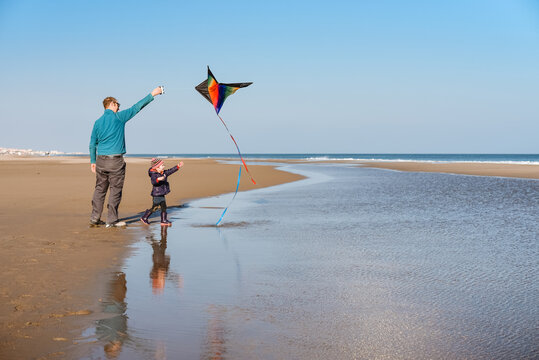 Father and child fly kite at beach on sunny winter day