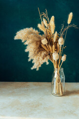 Bouquet of beige dried flowers in a glass vase on green blue background. Home decoration concept.
