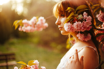 a red-haired girl with fringe looks curiously while standing between the flowers of a blossoming...