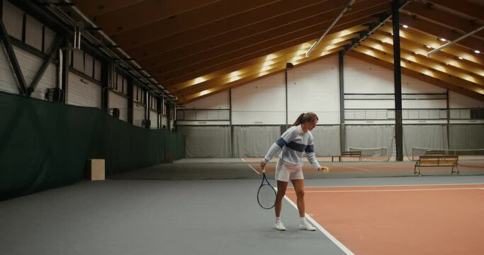 A woman starts a tennis set by hitting the ball playing in indoor tennis court