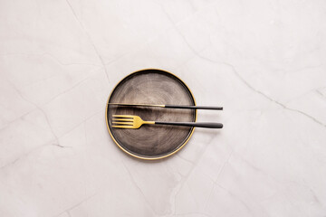 Top view image of vintage metal plate with golden cutlery with black handles on white marble table