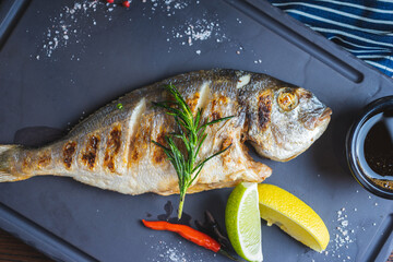 Grilled fish on a plate with a glass of wine and baked vegetables.