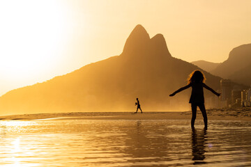 Kid playing on the water at Ipanema Beach, Brazil on a Sunset at summer. Two Brothers Mountain on...