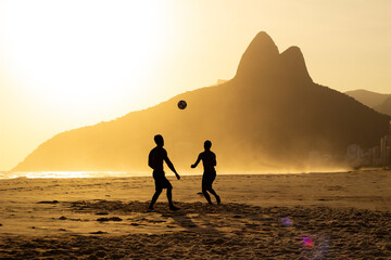 Two Brothers Mountain behind 2 friends playing soccer at Ipanema Beach, Rio de Janeiro. Sunset at summer - obrazy, fototapety, plakaty