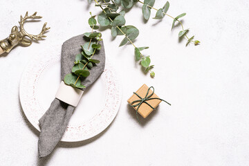 Festive table setting idea with white vintage plate, aromatic eucalyptus twigs and craft gift boxes on white rustic background top view. Eco friendly plastic free holidays concept.