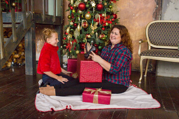 Obraz na płótnie Canvas Happy mom and daughter with a gift near the Christmas tree. Happy family. Mom and daughter are laughing. Christmas holidays.
