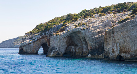 Cave in the rocky island cape in turquoise sea water with mountains on horison