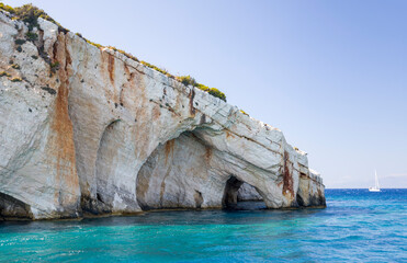 Cave in the rocky island cape in turquoise sea water with a yacht and mountains on horison and a cloud on the blue sky
