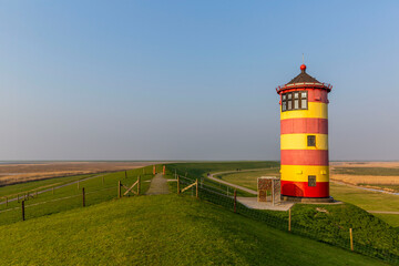 The striped red and yellow Pilsum lighthouse on the shores of the Wadden Sea in Germany