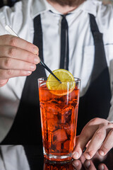 A professional bartender puts a slice of lemon in a red chilled alcoholic cocktail with bar tweezers in glass at a nightclub counter