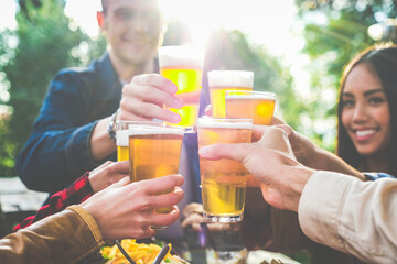 Group of multiethnic friends drinking beer at outdoor pub restaurant - Young people enjoying drinks during happy hour at terrace bar toasting with beers and chatting - Friendship concept