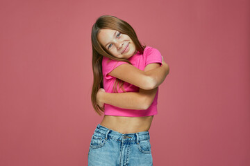 Smiling child girl embracing herself on pink background. Love and self acceptance. Healthy...