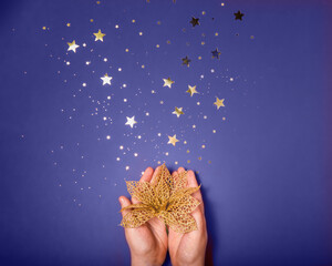 Female hands holding the golden decorative flower on purple background with gold stars sparkles.