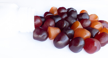 Group of red, orange and purple multivitamin gummies with the bottle isolated on white background. 