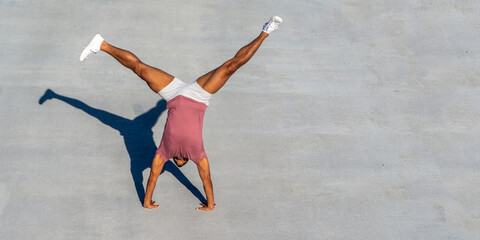 Multi-racial athletic male doing cartwheel with gray background.